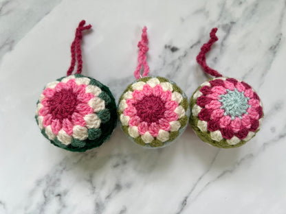 Three crocheted ornaments with pink and green patterns on a marble background