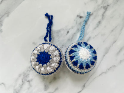 Two crocheted ornaments with blue and white patterns on a marble surface