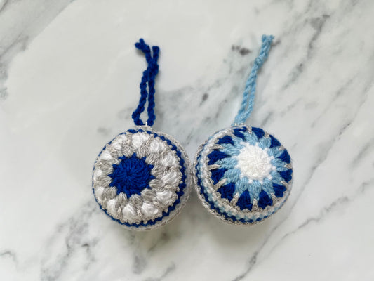 Two crocheted ornaments with blue and white patterns on a marble surface